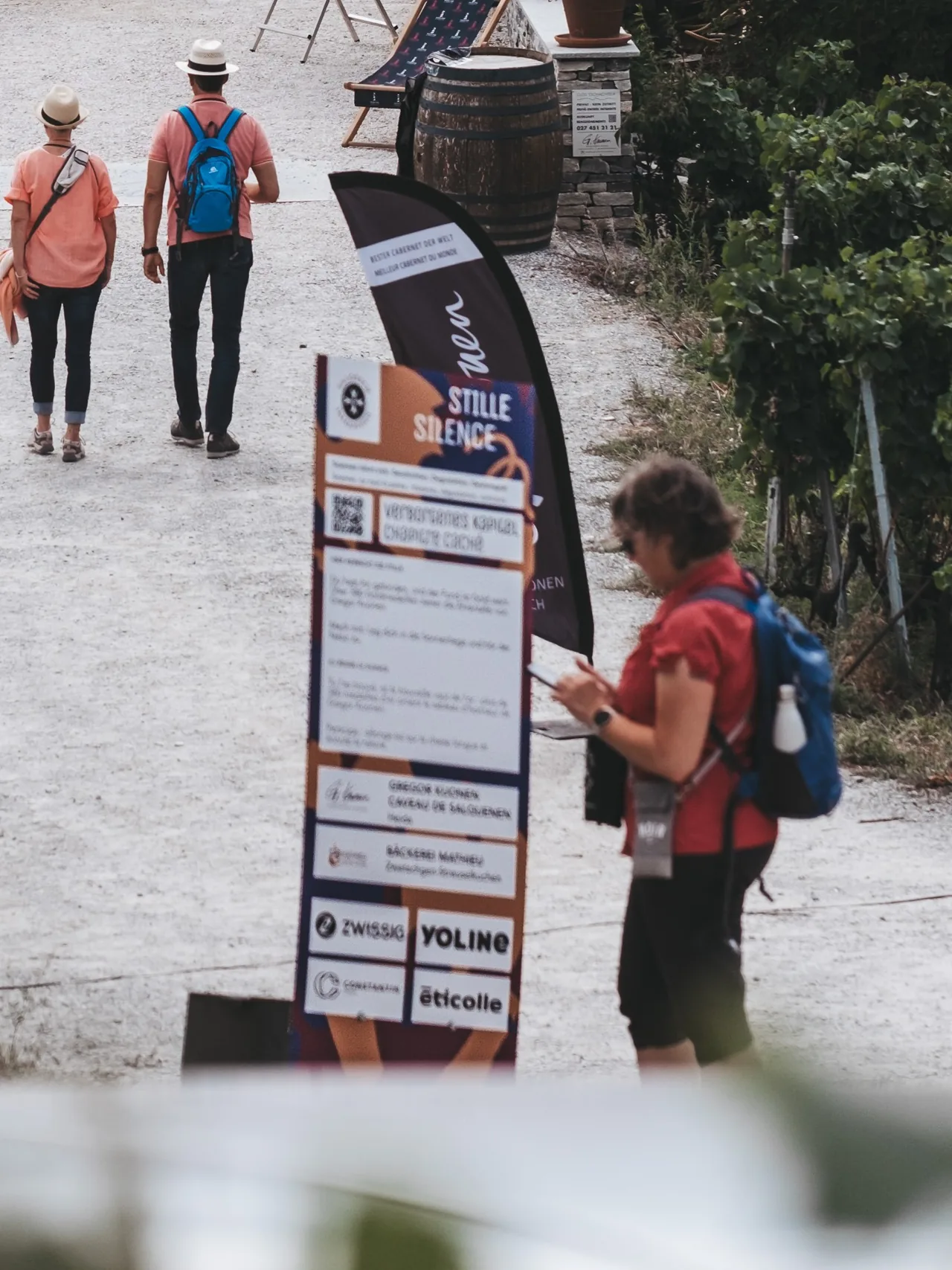 Wanderer an einer Stele mit QR-Code, eine Frau blickt auf ihr Telefon.
