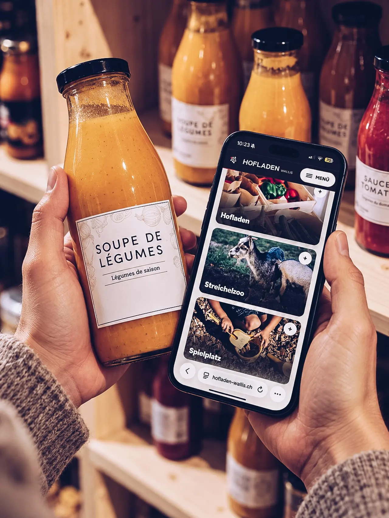 Hände halten eine Flasche Gemüsesuppe und ein Telefon mit der Hofladen-Website.
