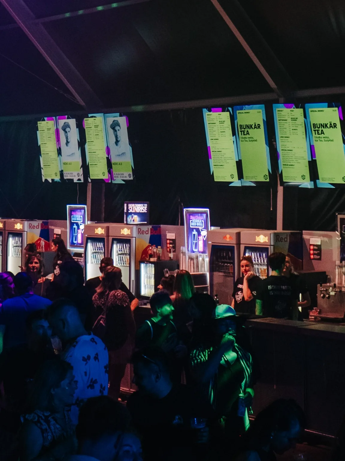 Leuchtende Bildschirme mit Getränkekarten über einer Festivalbar bei Nacht.