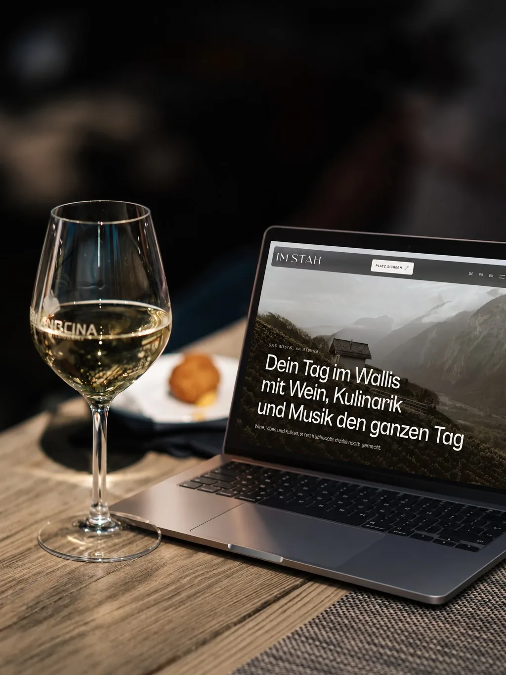 Ein Laptop mit einer Website zum Wallis, daneben ein Glas Weisswein.